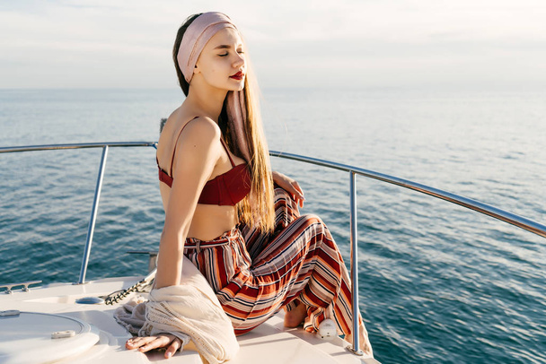 an attractive stylish girl in fashionable pants sits on a boat in the sun, relaxes and relaxes - Photo, image