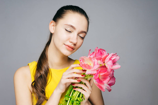 beautiful young woman enjoying the spring, holding pink flowers, closing her eyes - Photo, Image