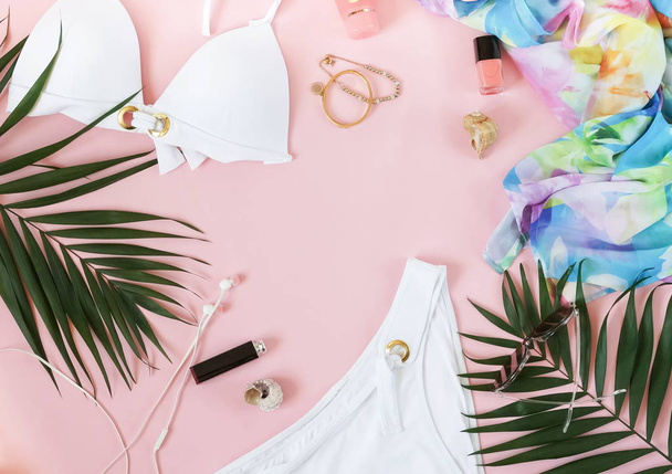 fashionable collage of female clothing for relaxation, a swimsuit, sunglasses, make up accessories and palm leaves on a pale pink background. Flat lay. top view. Copy space - Фото, изображение