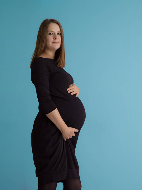 Portrait of happy pregnant woman with hands on belly isolated over blue background - Photo, Image