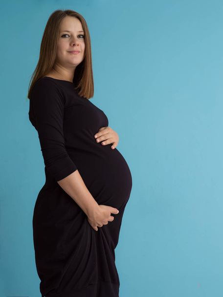 Portrait of happy pregnant woman with hands on belly isolated over blue background - Фото, изображение