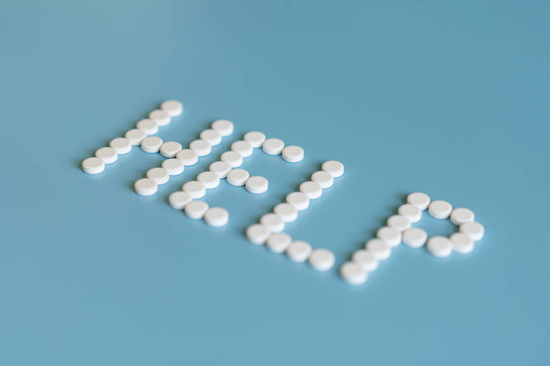 Fehér tabletták a kék háttér word súgójában. Fehér orvosi tabletták kék háttérrel. Súgó szó koncepció. - Fotó, kép