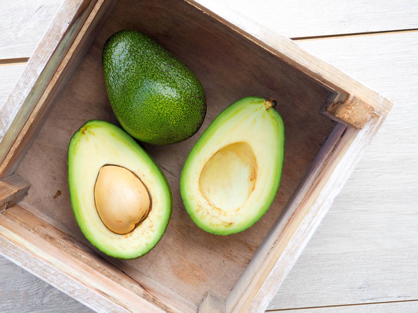 Avocado on old wooden table.Halfs on wooden bowl. Fruits healthy food concept. avocado in a wooden box. - Photo, Image