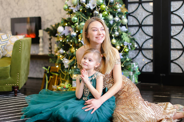 Young european happy mother and little daughter with bengal light sitting on floor near Christmas tree. - Фото, зображення