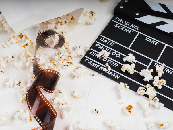 the film in the spiral, near the popcorn, Clapperboard copy space for text, fashion highlights in the photo, concept, film industry, film, abstract composition of movie, on a white background. - Photo, Image