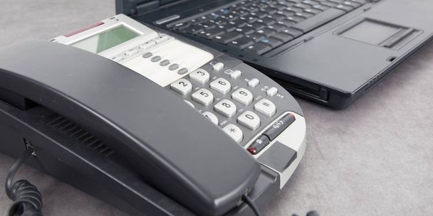 a black wired phone on the desk next to a laptop in office desk - Photo, Image
