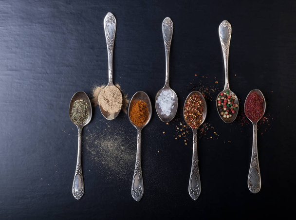 Old metal spoons with different kind of spices on a black background. - 写真・画像