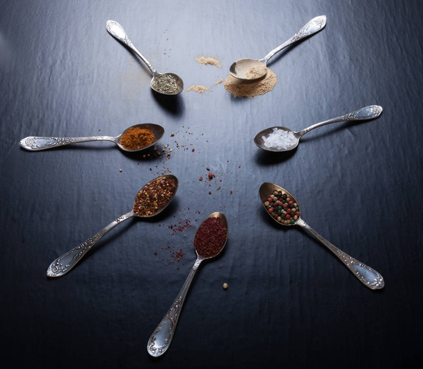 Old metal spoons with different kind of spices on a black background. Toned. - 写真・画像