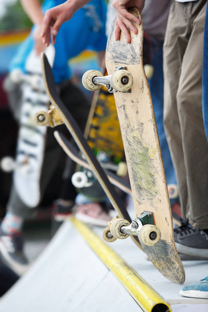 Skater boys ride on skate contest in park.Young athlete holds old skateboard in hand standing on plywood ramp top.Popular youth sport - 写真・画像