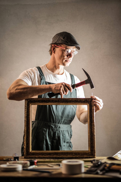 Craftsman fixing a picture frame with his hammer. - Fotó, kép