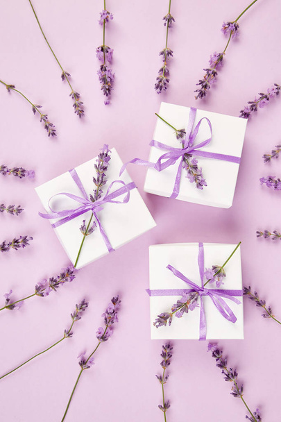 Caja de regalo blanca con cinta violeta y ramo de flores de lavanda sobre fondo rosa. Celebración, cumpleaños. Regalo de decoración. Acostado. Copiar espacio
. - Foto, imagen
