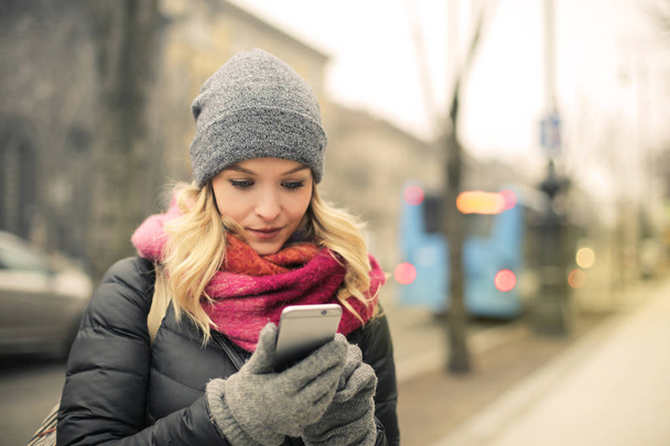 Blonde woman checking her smartphone in winter on the street in the city. - Foto, afbeelding