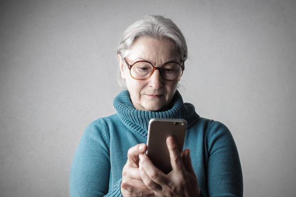 Old lady with glasses checking her smartphone indoor. - Photo, image