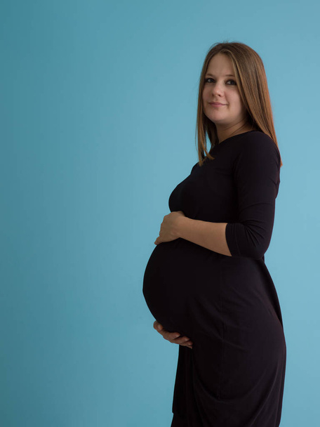 Retrato de mulher grávida feliz com as mãos na barriga isolada sobre fundo azul
 - Foto, Imagem