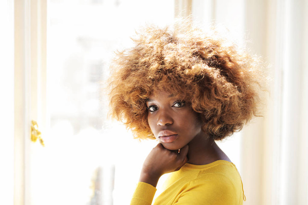 Young beautiful black woman in a yellow sweater indoor. - Foto, afbeelding