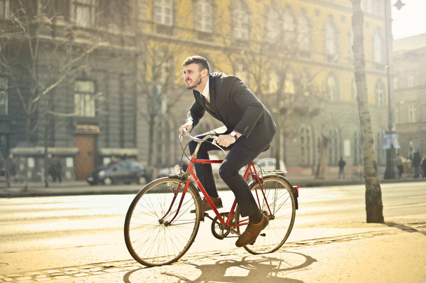 Young businessman on a bike in a hurry in the city. - Foto, afbeelding