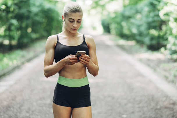 Donna Runner nel Summer Morning Park Ascoltare musica su smartphone utilizzando auricolari Bluetooth. femmina fitness ragazza jogging su percorso al di fuori
. - Foto, immagini