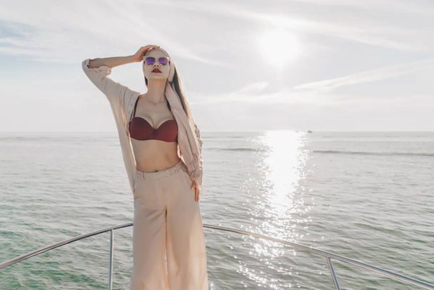 a luxurious stylish girl in summer clothes enjoys a sea voyage on a yacht, in the rays of the sun - Photo, Image