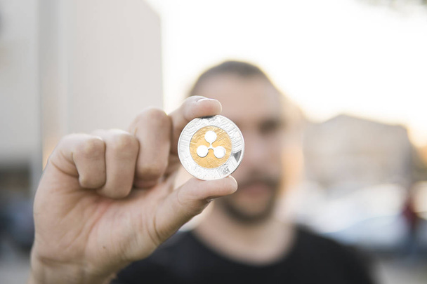 Golden silver Ripple coin in hand on a blurred sunset background with a man. Hand holding a crypto currency virtual money. Bussiness, commercial, exchange, digital money. - Φωτογραφία, εικόνα