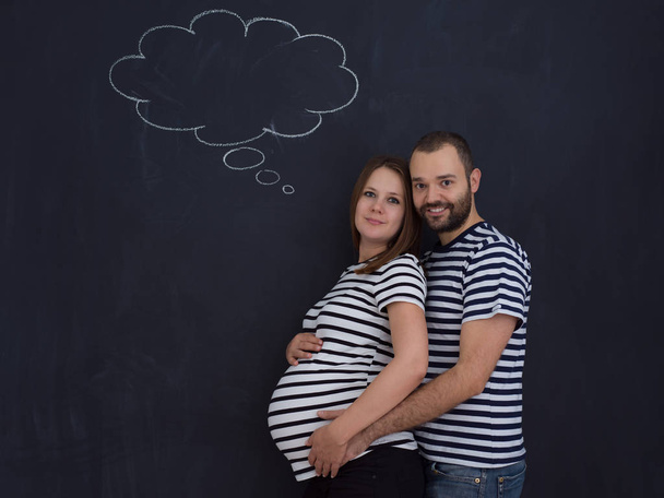portrait of husband and pregnant wife posing against black chalk drawing board - Фото, зображення