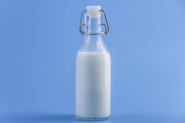 Γυάλινο μπουκάλι με το φρέσκο γάλα σε μπλε φόντο. Πολύχρωμο μινιμαλισμό. Η έννοια του υγιούς γαλακτοκομικά προϊόντα με ασβέστιο - Φωτογραφία, εικόνα
