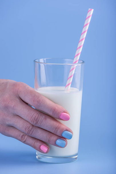 Женская рука держит стакан свежего молока с соломинкой на синем фоне. Красочный минимализм. Концепция здоровых молочных продуктов с кальцием
 - Фото, изображение