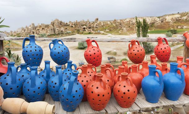 Des pots de désirs en argile bleue et rouge se dressent sur une table grossière en bois faite de planches altérées sur fond de grottes de Cappadoce
. - Photo, image