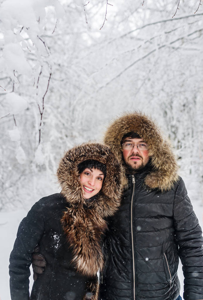 Portrait of a smiling young couple in fur hood jackets in the winter forest. - Photo, Image
