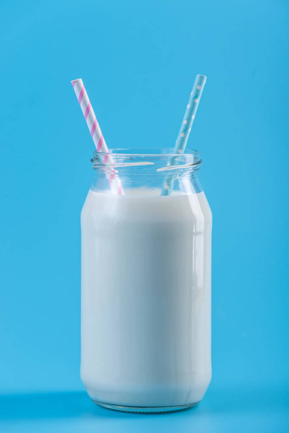 Bottiglia di vetro di latte fresco con due cannucce su fondo blu. Minimalismo colorato. Il concetto di latticini sani con calcio
 - Foto, immagini