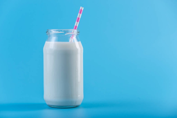 Botella de vidrio de leche fresca con paja sobre fondo azul. Minimalismo colorido. El concepto de productos lácteos saludables con calcio
 - Foto, Imagen