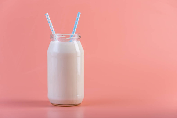 Glass bottle of fresh milk with two straws on pink background. Colorful minimalism. The concept of healthy dairy products with calcium - Photo, image