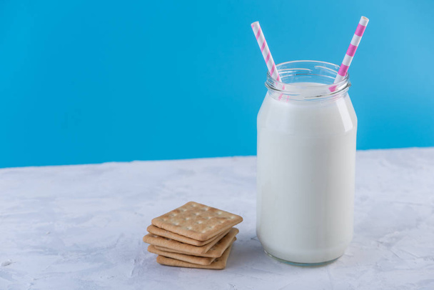 Glass bottle of fresh milk with straw and cookies on blue background. Colorful minimalism. The concept of healthy dairy products with calcium - Фото, изображение