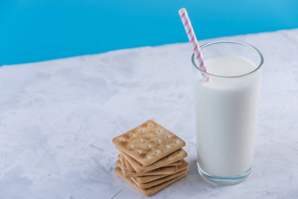Een glas verse melk met een rietje en cookies op een blauwe achtergrond. Kleurrijke minimalisme. Het concept van gezonde zuivelproducten met calcium - Foto, afbeelding