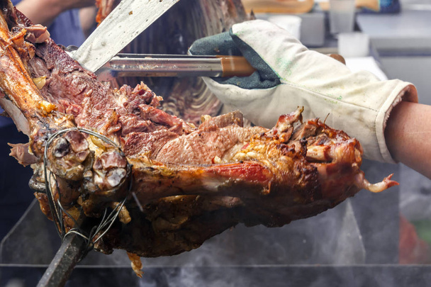 Hand cook with a knife and forceps cut into pieces the ready lamb on a spit over hot coals. Outdoor grill - Photo, Image