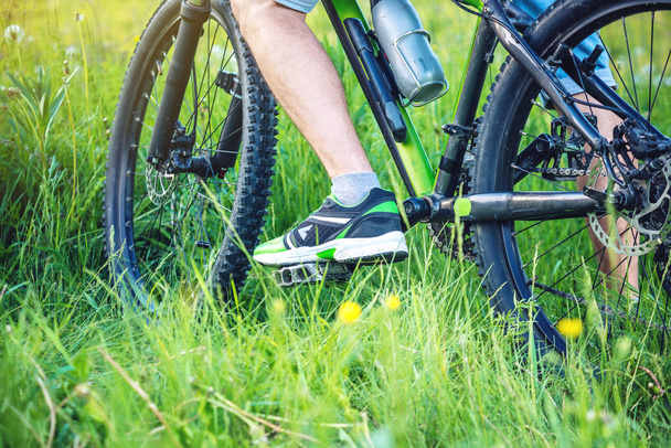 Велосипедист на зеленом горном велосипеде в лесу верхом на траве. Вид снизу и сзади. Понятие активного и экстремального образа жизни
 - Фото, изображение