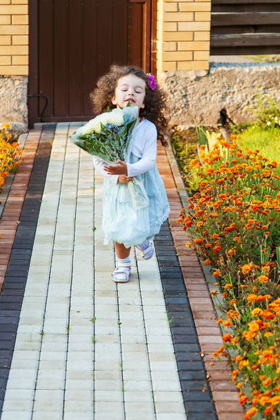 Маленька дівчинка з букетом квітів біжить на прогулянці у дворі будинку
 - Фото, зображення