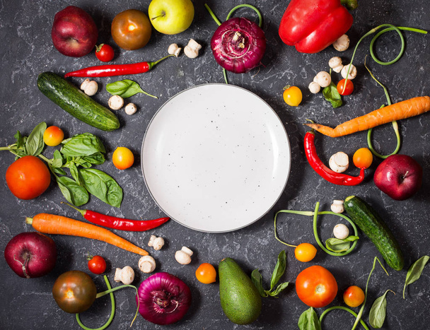 Verduras orgánicas frescas e ingredientes de condimento para una sabrosa cocina vegetariana alrededor de un plato blanco en blanco, vista superior
. - Foto, Imagen