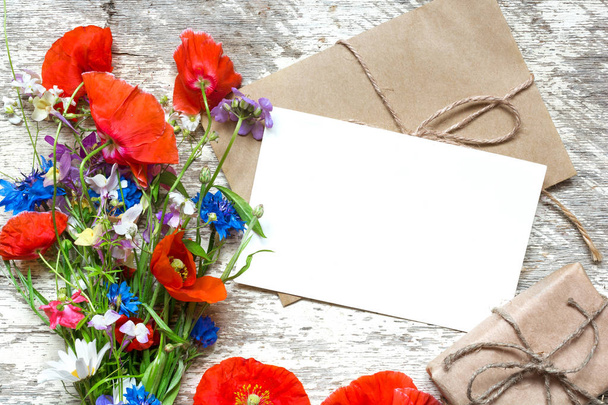 biglietto di auguri bianco vuoto con mazzo di fiori selvatici estivi e scatola regalo su sfondo in legno rustico. vista dall'alto. prendere in giro
 - Foto, immagini