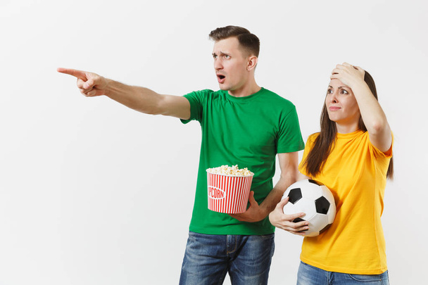 Незадоволена пара, жінка, чоловік, шанувальники футболу в жовтій зеленій футболці підбадьорюють команду підтримки з футбольним м'ячем попкорну ізольовано на білому тлі. Спорт, сімейне дозвілля, концепція способу життя
 - Фото, зображення