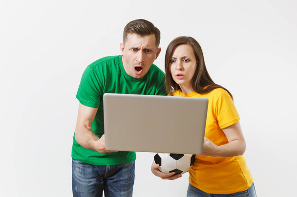 Шокована пара жінка чоловік, футбольні фанати в жовтій зеленій футболці підбадьорюють команду підтримки з футбольним м'ячем, спостерігаючи за грою на ноутбуці ПК ізольовано на білому тлі. Концепція спортивного сімейного дозвілля
 - Фото, зображення
