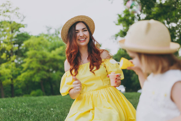 Laughing woman in yellow clothes play in park rest and have fun with little cute child baby girl hold soap bubble blower. Mother, little kid daughter. Mother's Day, love family, parenthood, childhood - Photo, Image