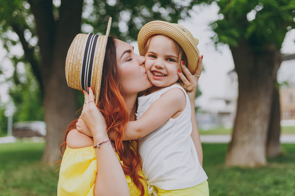 Attractive woman in yellow clothes kiss and hug, embrace with little cute child baby girl play, have fun in green park. Mother, little kid daughter. Mother's Day, love family, parenthood, childhood - Foto, Bild