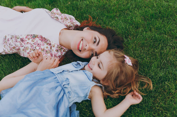 Smiling tender woman in light dress and little cute child baby girl lie on green grass in park rest, have fun. Mother, little kid daughter. Mother's Day, love family, parenthood, childhood concept - Photo, Image