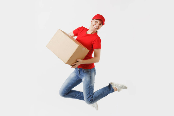Full length portrait of fun delivery woman in red cap, t-shirt isolated on white background. Female courier or dealer jumping with empty cardboard box. Receiving package. Copy space for advertisement - Photo, Image