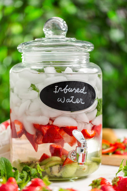 Agua infundida con fresas orgánicas, kiwi y menta fresca en dispensador de bebidas de vidrio
. - Foto, imagen