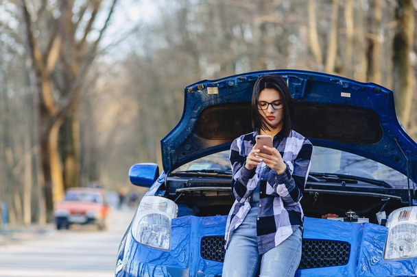 ελκυστική κοπέλα με το τηλέφωνο κοντά στο ανοιχτό καπό του αυτοκινήτου στο δρόμο - Φωτογραφία, εικόνα