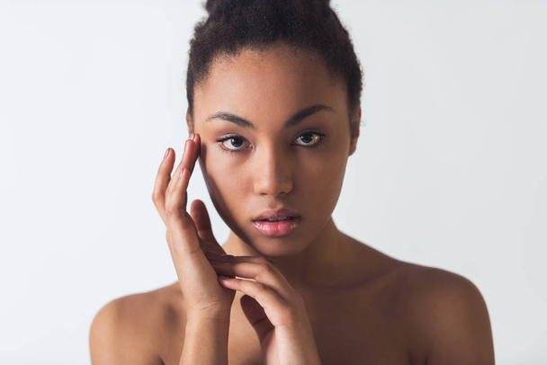Красивая афро-американская девушка прикасается к лицу и смотрит в камеру, изолированную на белом
 - Фото, изображение