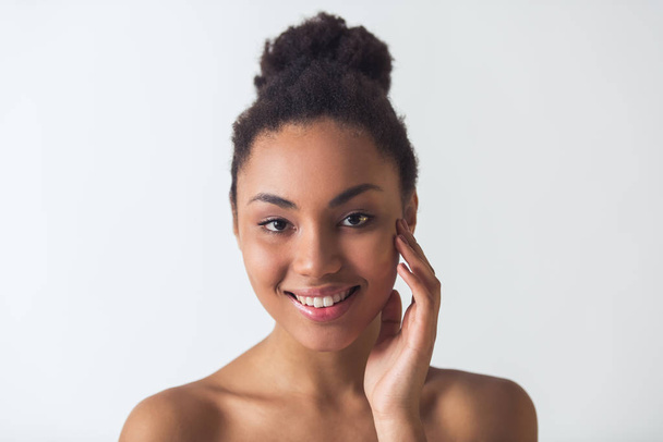 Bella ragazza afro-americana si sta toccando il viso, guardando la fotocamera e sorridendo, isolato su bianco
 - Foto, immagini