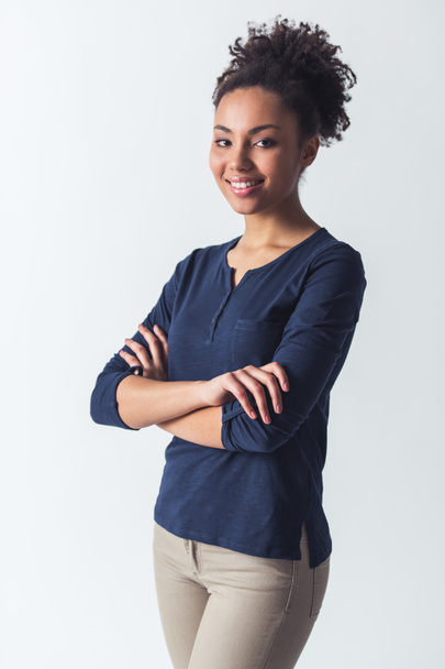 Όμορφο κορίτσι αφρο-αμερικανικό casual ρούχα κοιτάζοντας κάμερα και χαμογελώντας ενώ στέκεται με σταυρωμένα χέρια, απομονώνονται σε λευκό - Φωτογραφία, εικόνα
