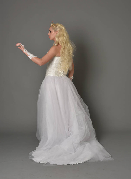 Pełna długość Portret Blondynka dziewczyna ubrana w suknię biały fantasy. pozie stojącej w strony profilu, szary studio tło. - Zdjęcie, obraz